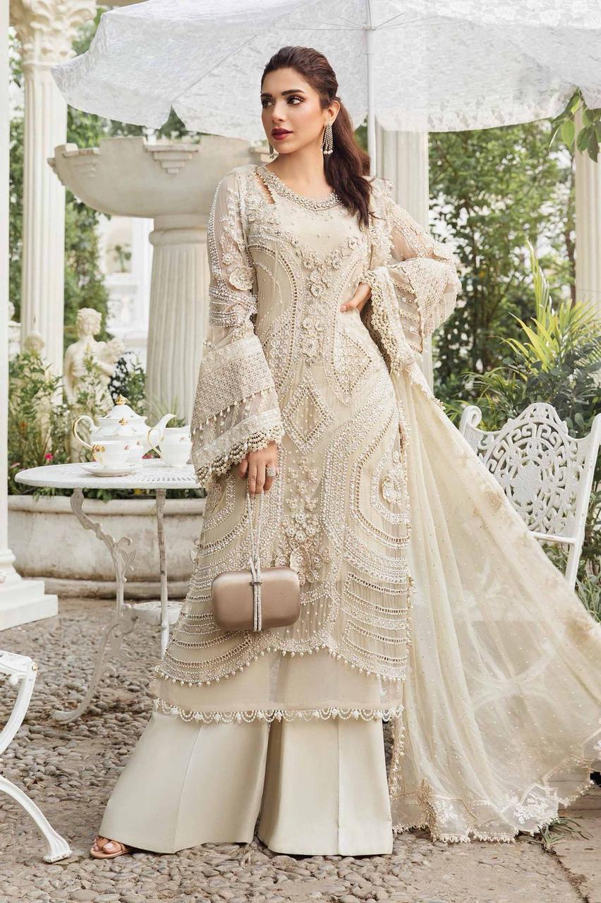 Woman in a cream embroidered traditional outfit standing in an elegant outdoor setting.