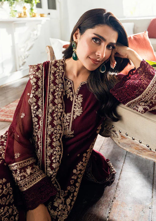 Woman in traditional maroon and gold embroidered outfit sitting on a couch.