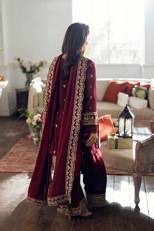 Woman in a maroon traditional outfit with gold embroidery standing in a living room.