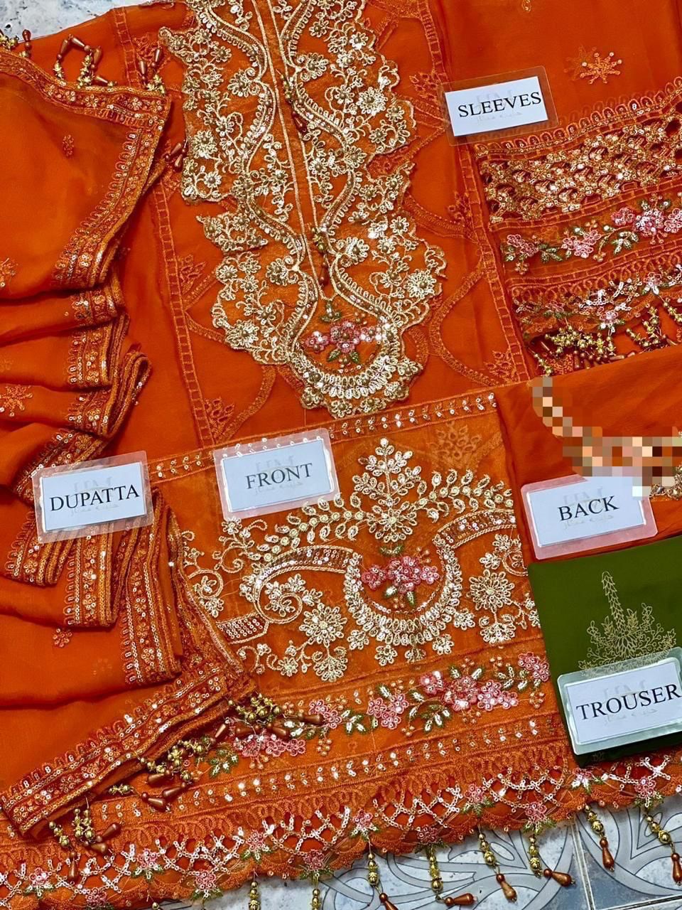 Orange embroidered fabric with labels indicating parts of a traditional outfit.