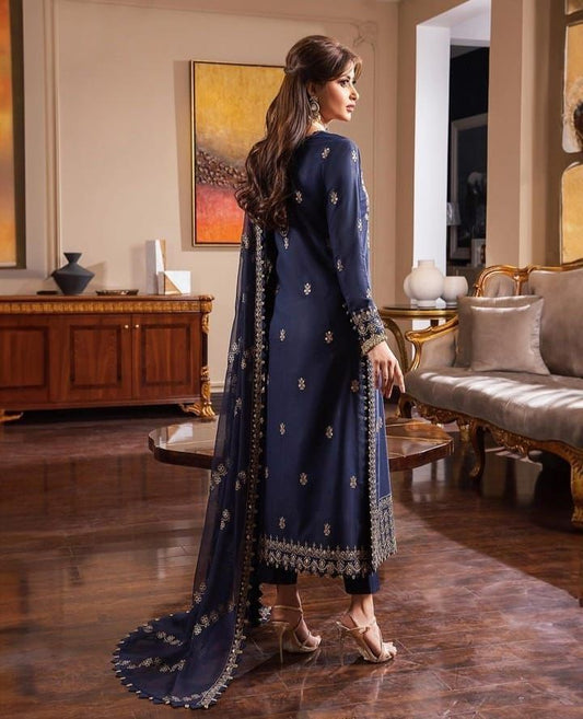 Woman in a navy blue embroidered outfit standing in a stylish room.