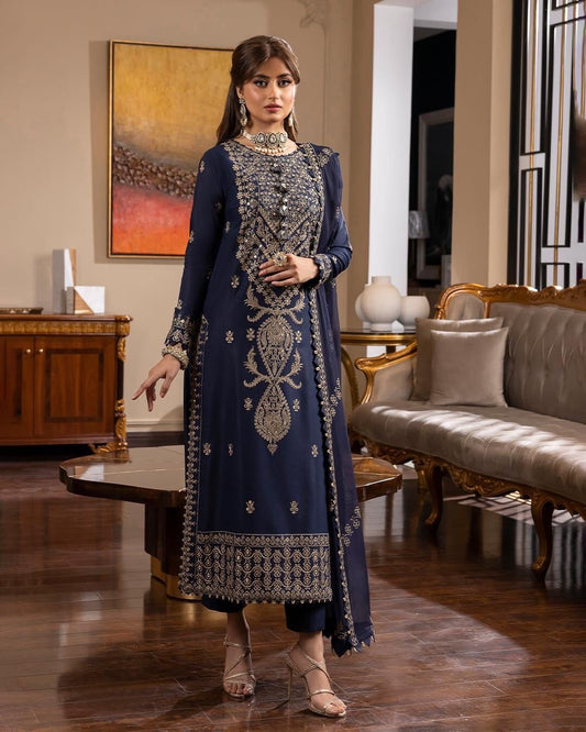 Woman in a blue embroidered traditional outfit standing in an elegant room.