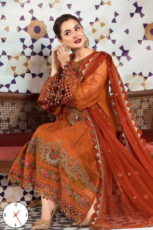 Woman in an orange embroidered traditional outfit sitting against a patterned wall.